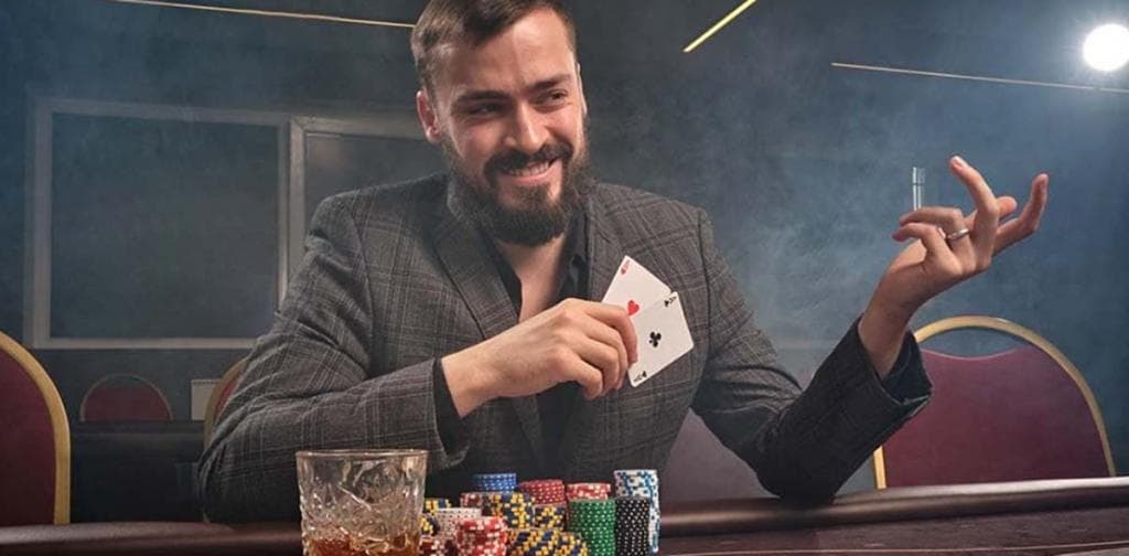 Mosolygó játékos ász és bubi kártyával, pókerasztal zsetonokkal és whiskyvel kaszinóban.