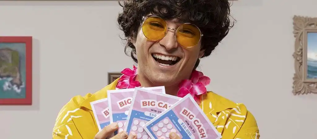 Mosolygó férfi sárga ingben, rózsaszín virágfüzérrel, kezében négy BIG CASH kaparós sorsjegyet tartva.