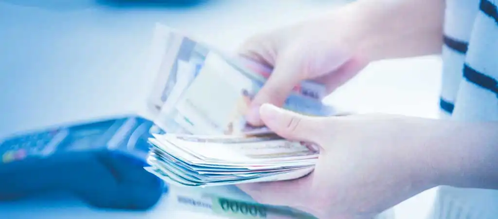 Két kéz, amely magyar forint bankjegyeket számol egy fizetési terminál mellett, szerencsejáték és pénz témában.