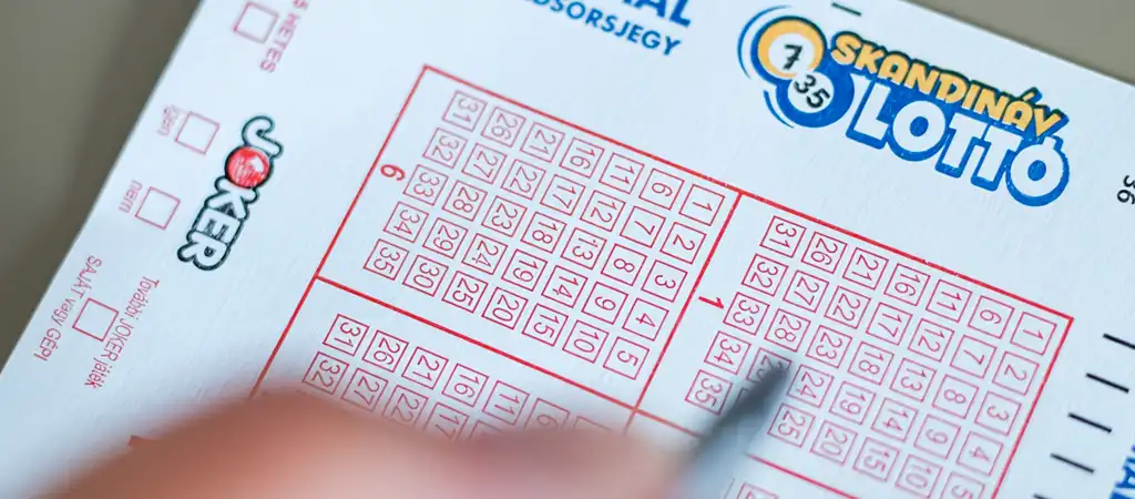 Skandináv lottószelvényt tölt ki egy kéz tollal.